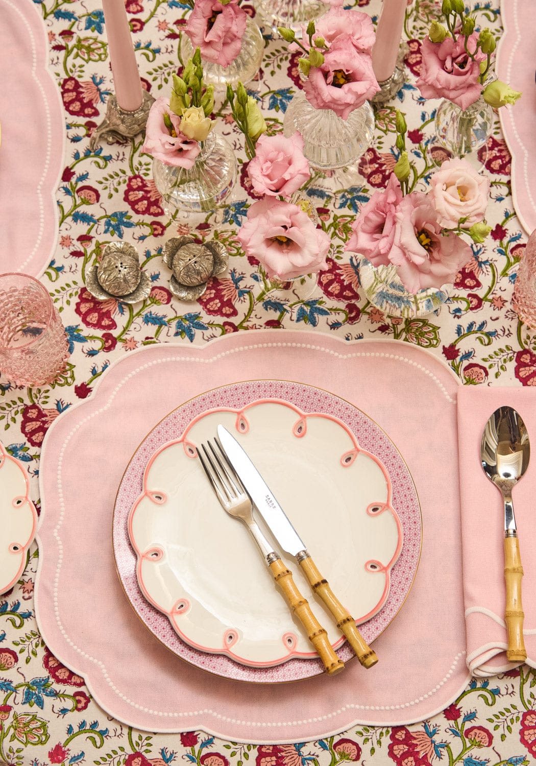 Table setting with pink plates, floral tablecloth, and cutlery on a decorative table.
