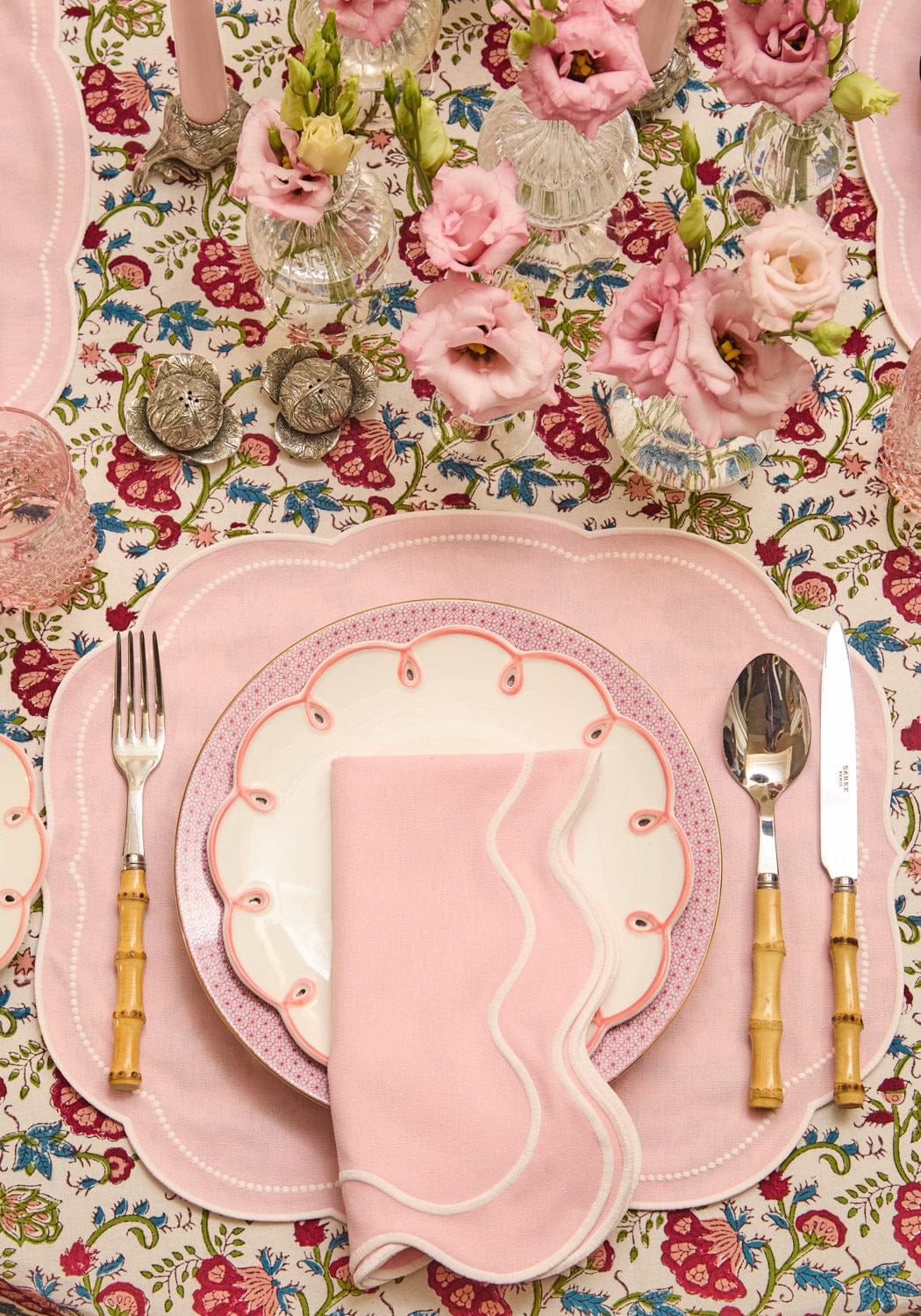Pink scalloped plates with floral tablecloth and cutlery with cabbage salt and pepper shakers