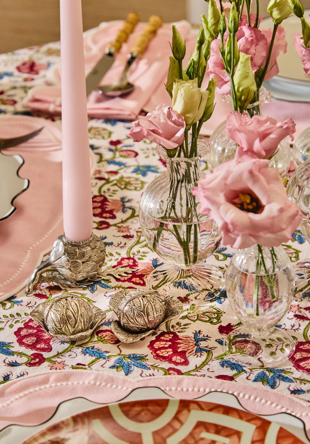 Decorative table setting with pink candles, floral arrangements, and a patterned tablecloth with cabbage salt and pepper seasoners.