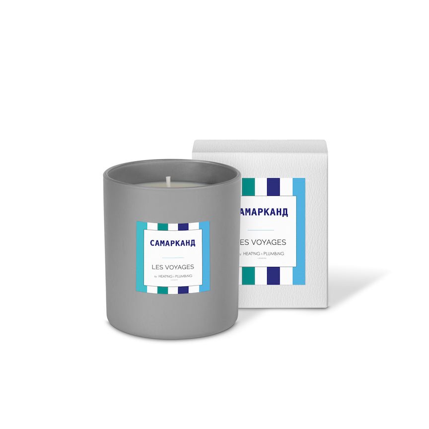 Grey candle with a label next to its packaging on a white background