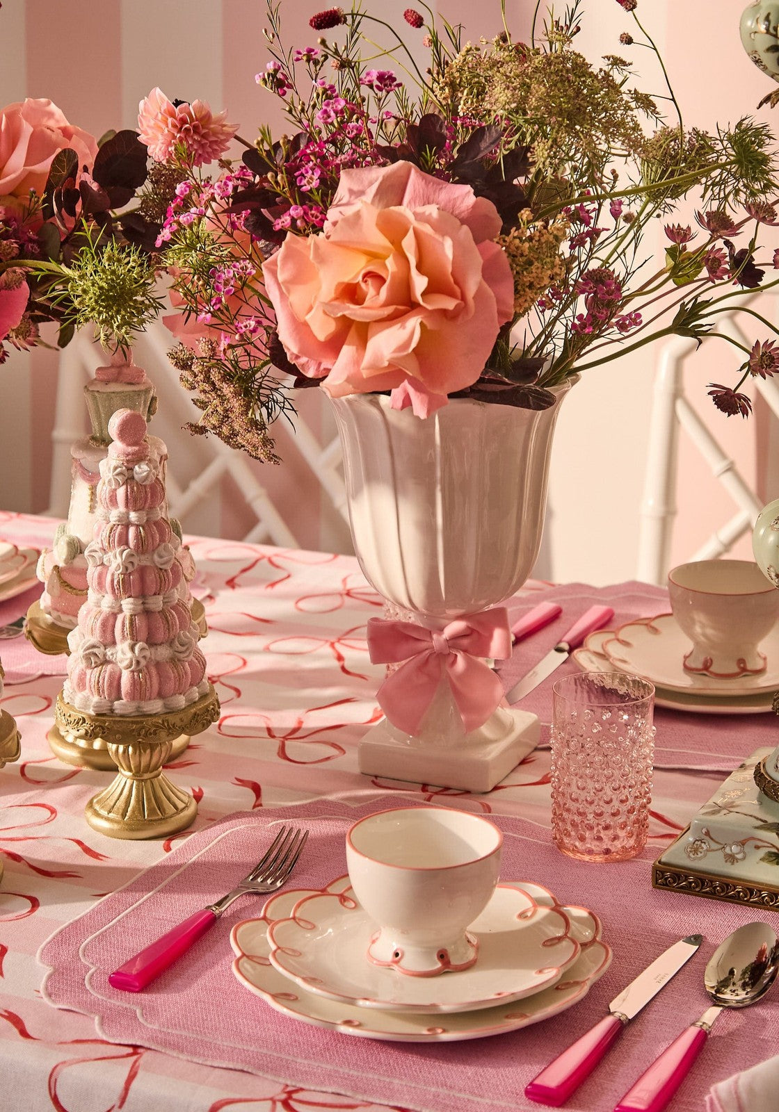 Decorative table setting with pink floral arrangement, teacups, and tableware on a pink tablecloth.