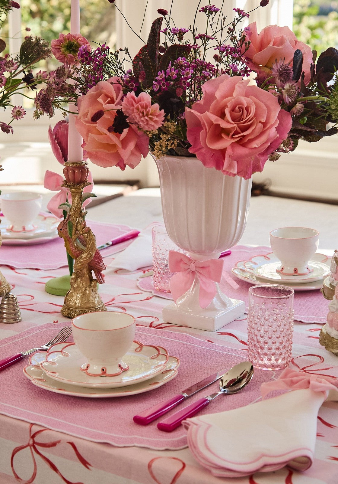 Decorative table setting with pink flowers, cups, and a pink tablecloth.