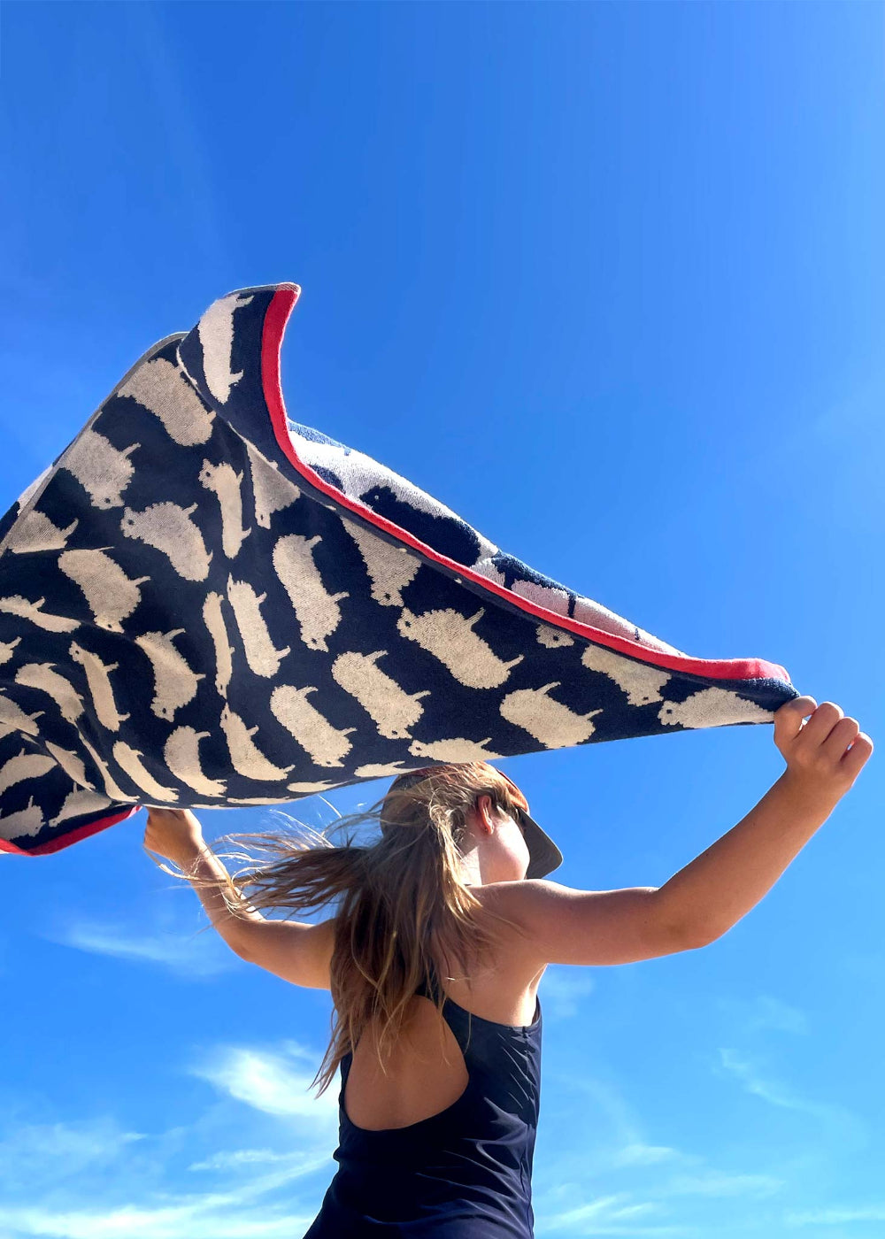 Person holding a patterned towel with sheep against a blue sky
