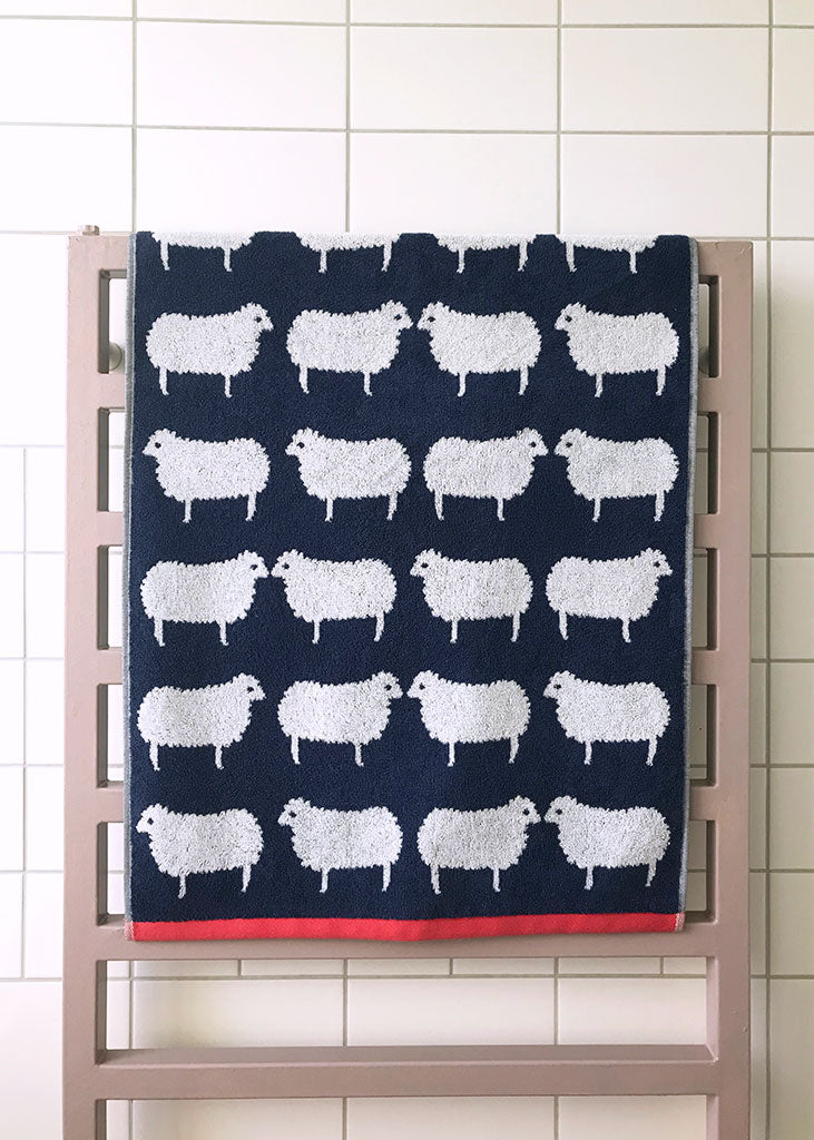 Navy towel with white sheep pattern hanging on a rack against a tiled wall.