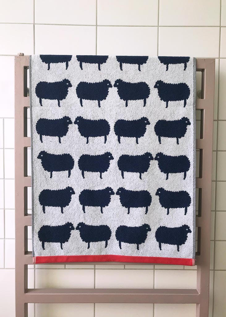 Towel with black sheep pattern on a wooden rack against a tiled wall.