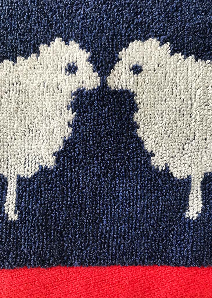 Close-up of bath towels with white and navy sheep pattern on a red background