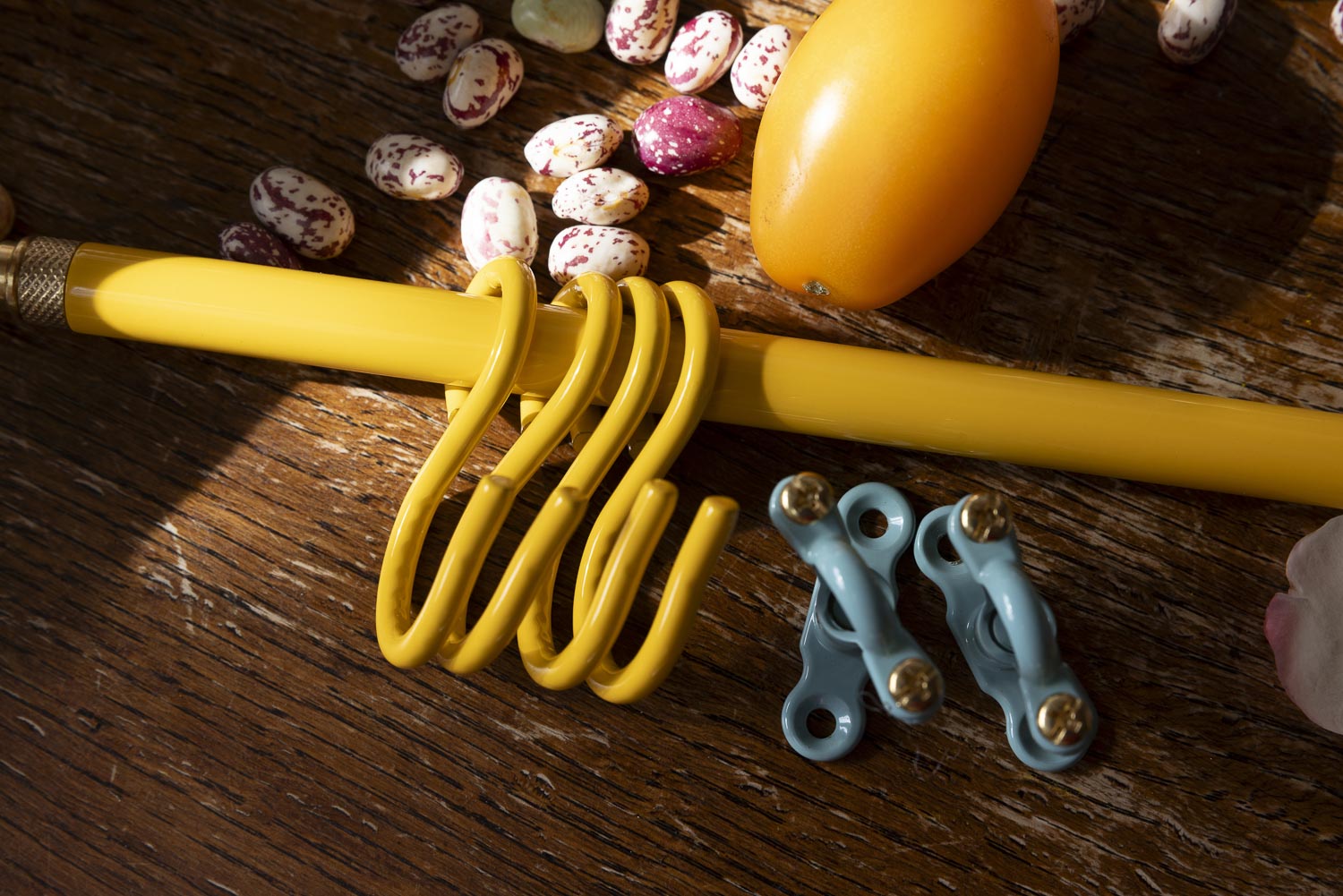 A yellow metal kitchen hanging rail set displayed on a rustic wooden surface, including a long horizontal hanger draped across a yellow pencil, a coiled U-shaped hanger, and two smaller light blue hangers with gold-toned hardware.