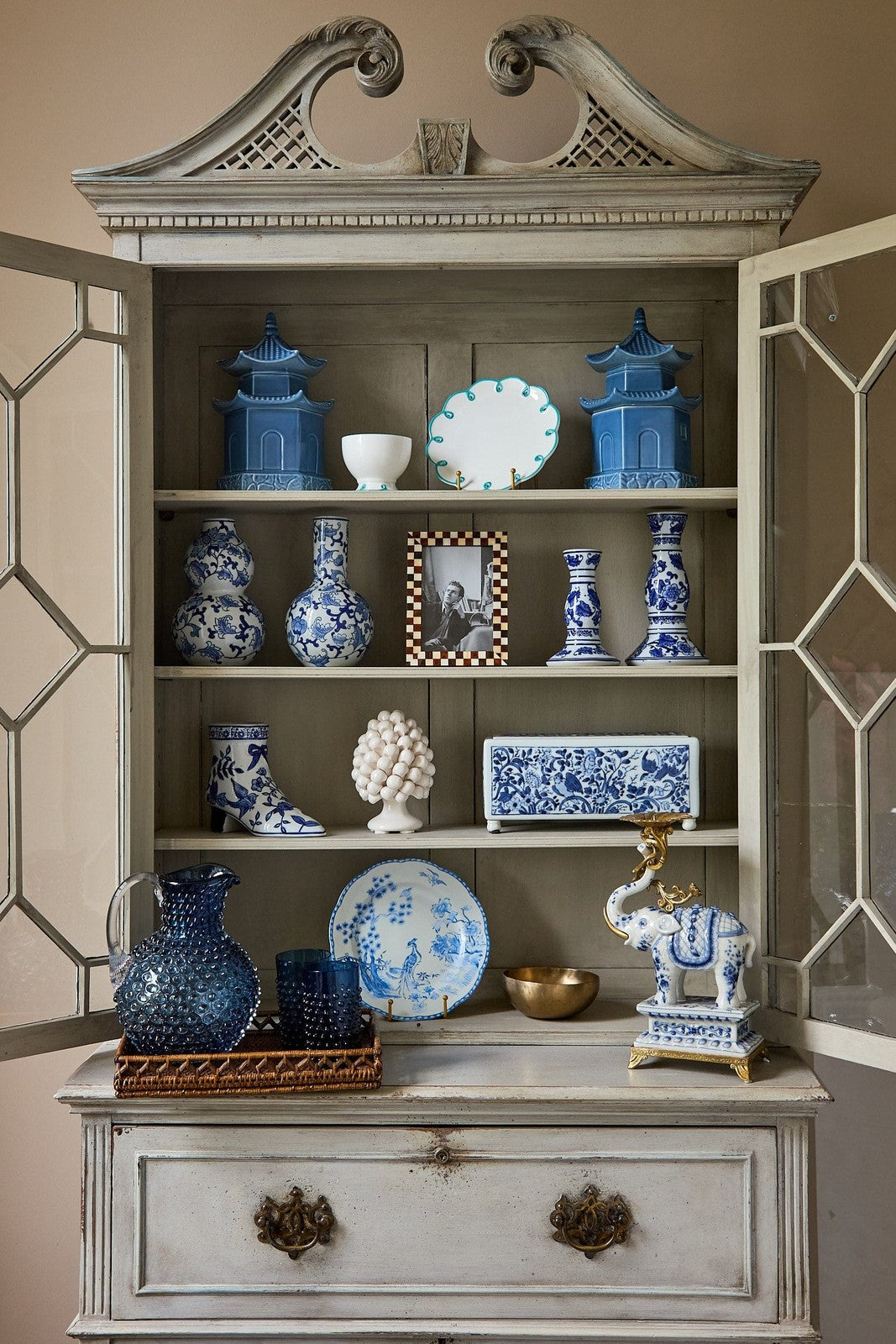 Decorative cabinet with blue and white ceramic items against a neutral wall.