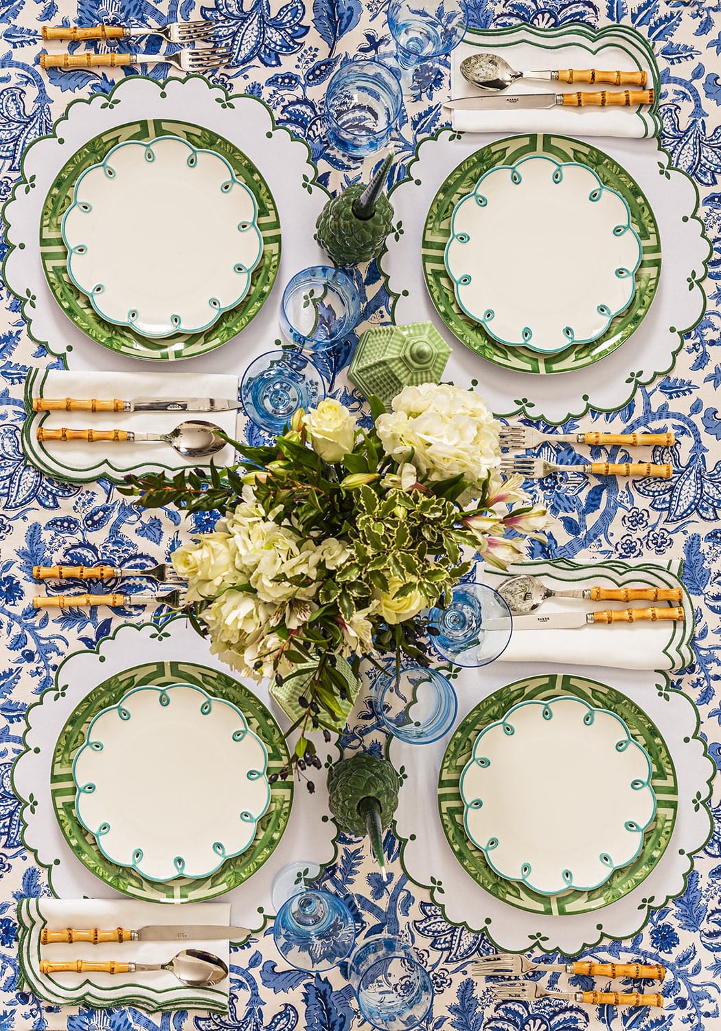 Elegant table setting with green and white plates, silverware, and a floral centerpiece on a blue and white patterned tablecloth.