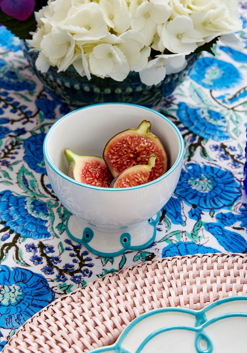 Scalloped edge Bowl of figs on a decorative tablecloth with flowers in the background