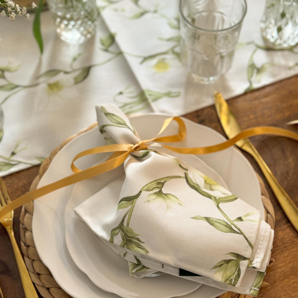 Table setting with floral napkins, gold cutlery, and glasses on a wooden table.