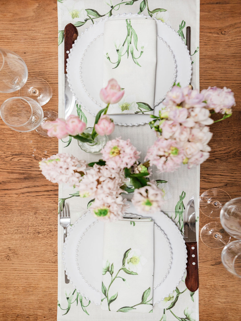 Table setting with floral table runner, plates, and glasses on a wooden table.
