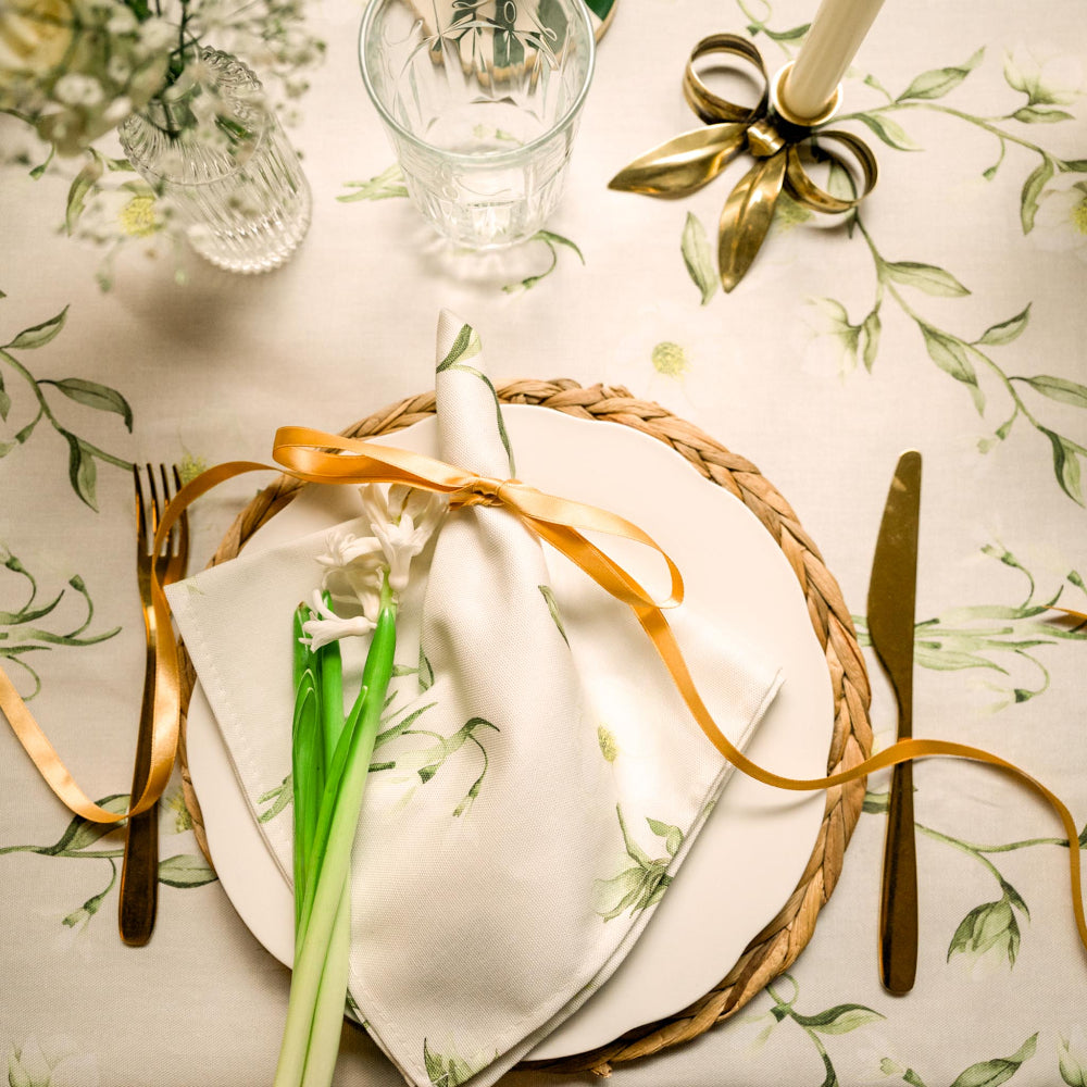 Elegant table setting with gold ribbon, white napkin, and floral-patterned tablecloth.