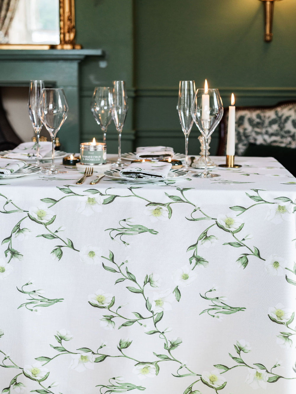 Dining table set with floral-patterned tablecloth, wine glasses, and candles in a formal setting.