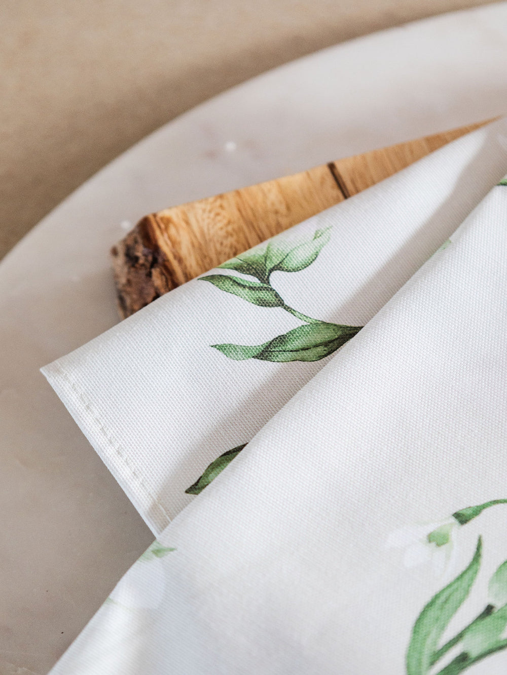 White tea towel with green leaf snowdrop pattern on a beige background