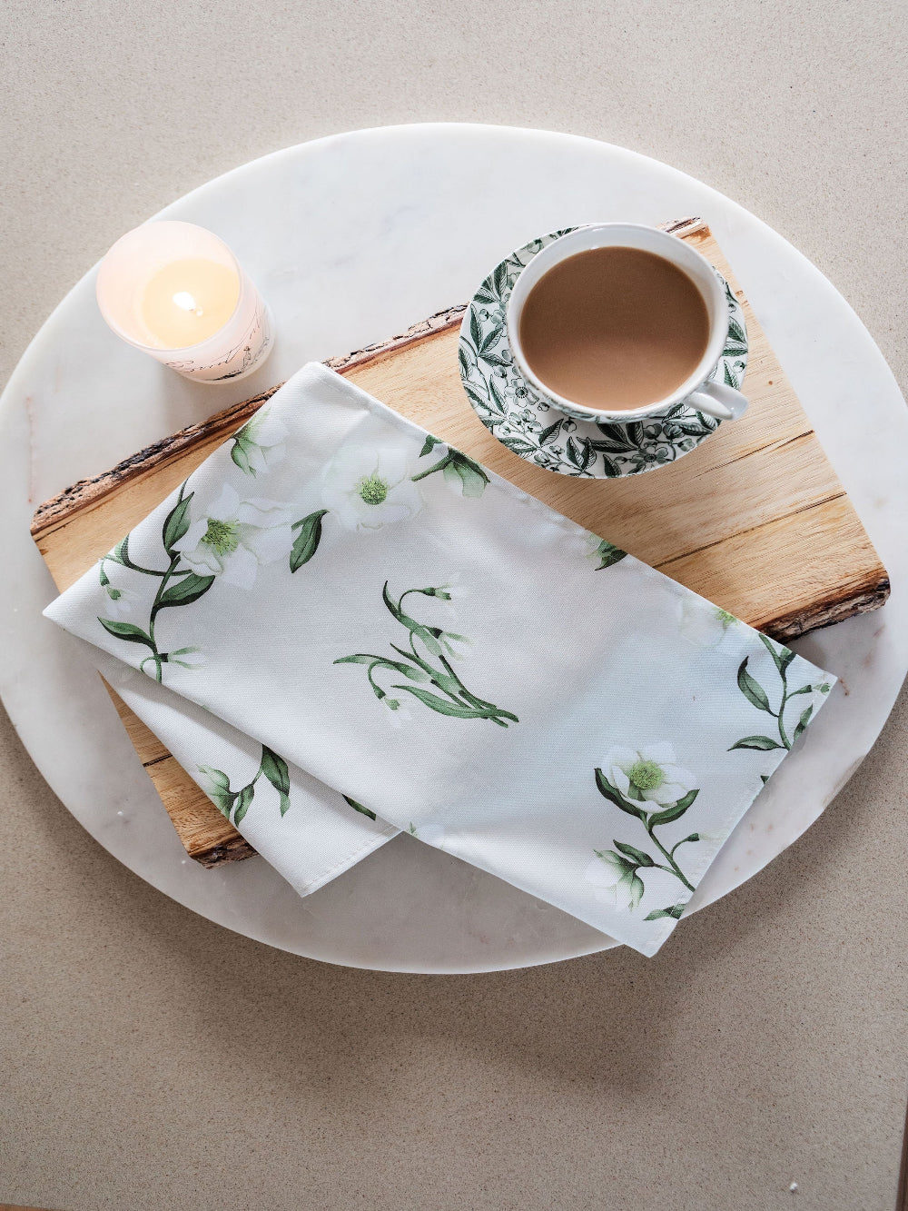 Tea Towel with green leaf pattern on a wooden cutting board with a cup of coffee and candle.