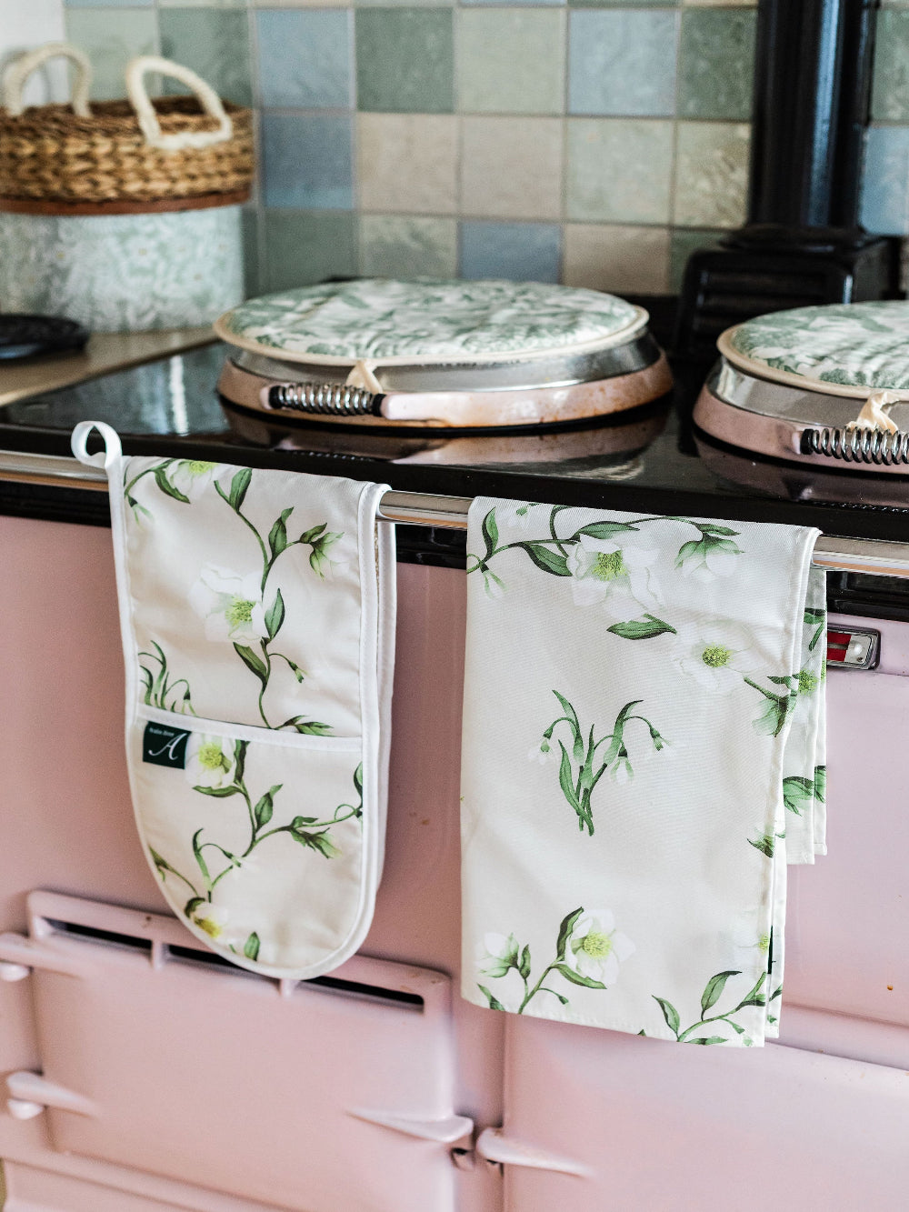 Pink Aga range cooker with floral-patterned oven mittens and tea towel hanging on the handle.