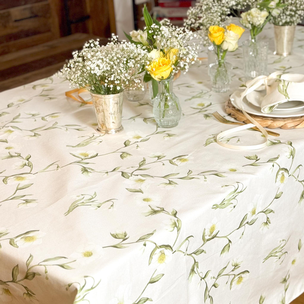 Table setting with floral tablecloth, flowers, and silverware on a wooden table.