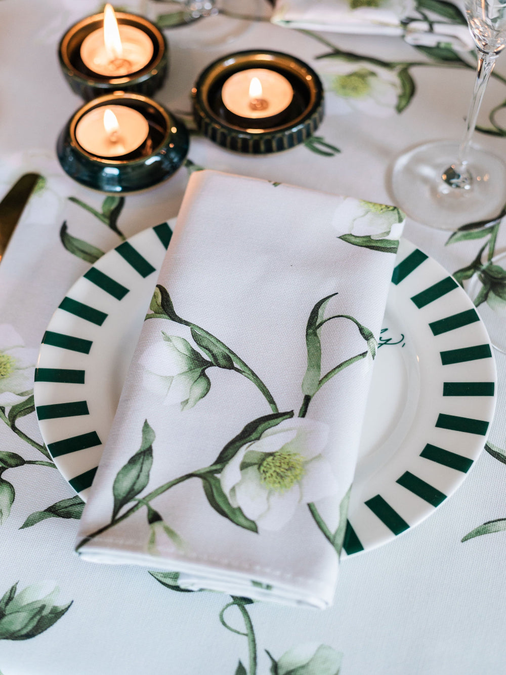 Table setting with floral-patterned plates, napkin, and candles on a matching tablecloth.