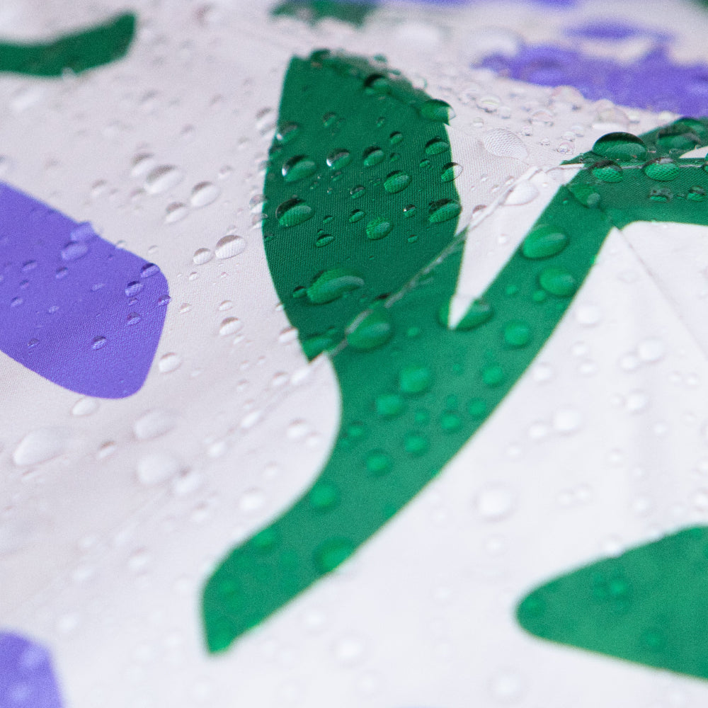 Close-up of an umbrella with green and purple flower shapes and water droplets.
