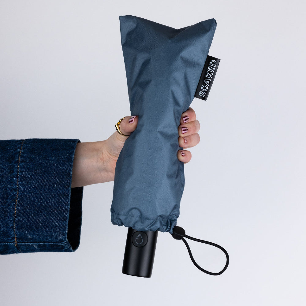 Folded blue umbrella held by a hand with a white background