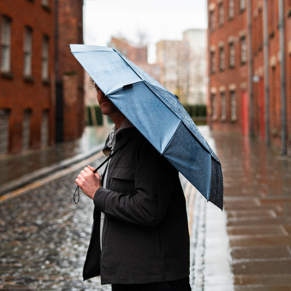 Person holding a blue umbrella walking down a rain-soaked street with brick buildings.