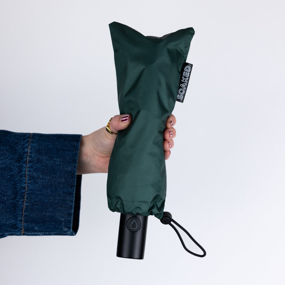 Green umbrella with black handle held by a person against a white background