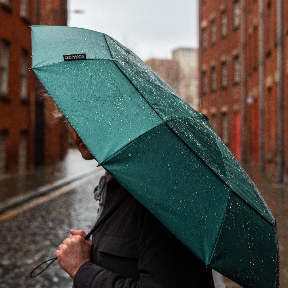 Person holding a green umbrella in a rainy street with brick buildings.
