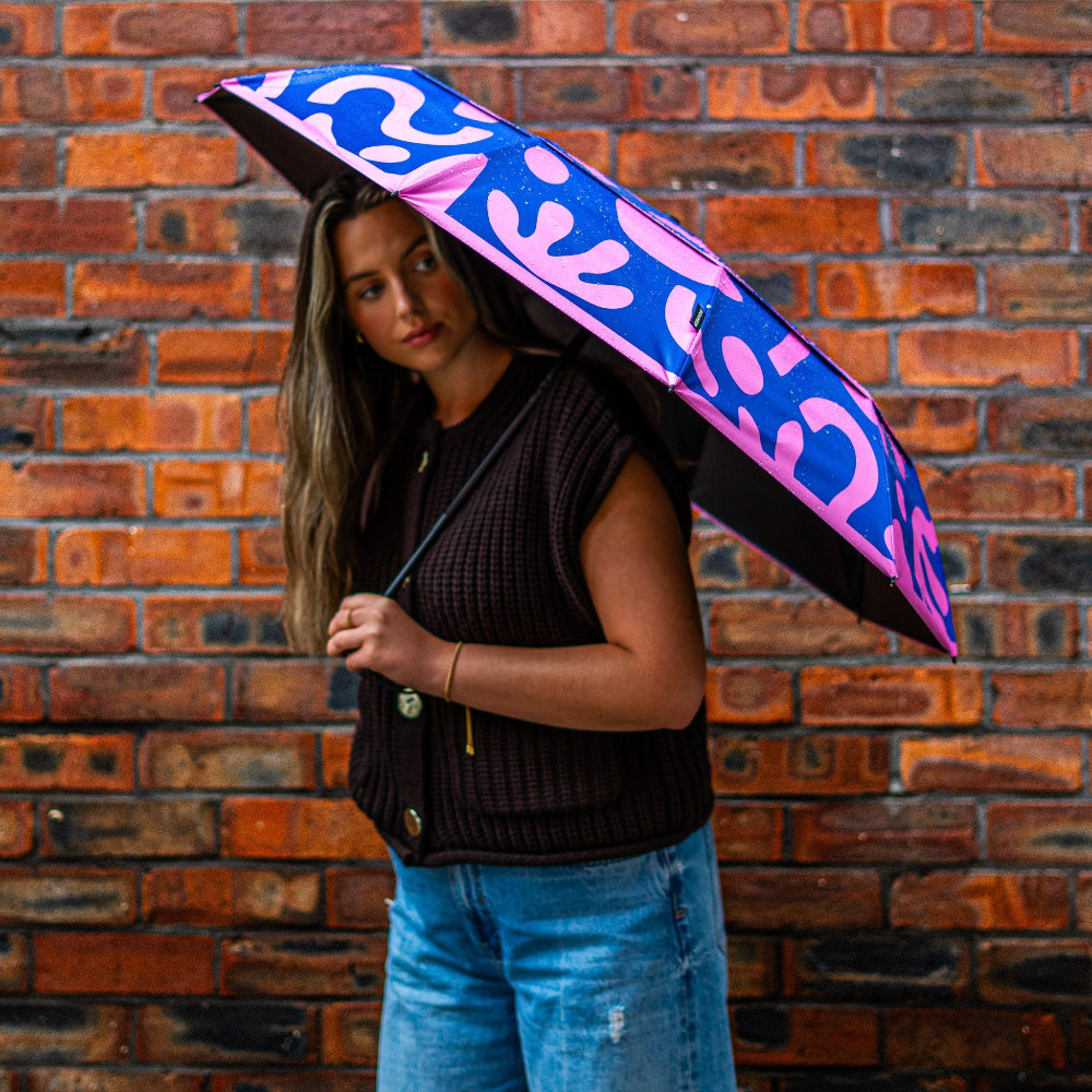 Person holding a colourful umbrella against a brick wall