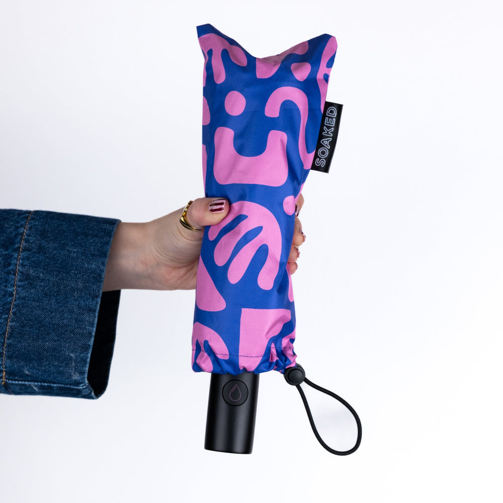 Hand holding a blue and pink patterned umbrella with a black handle on a white background
