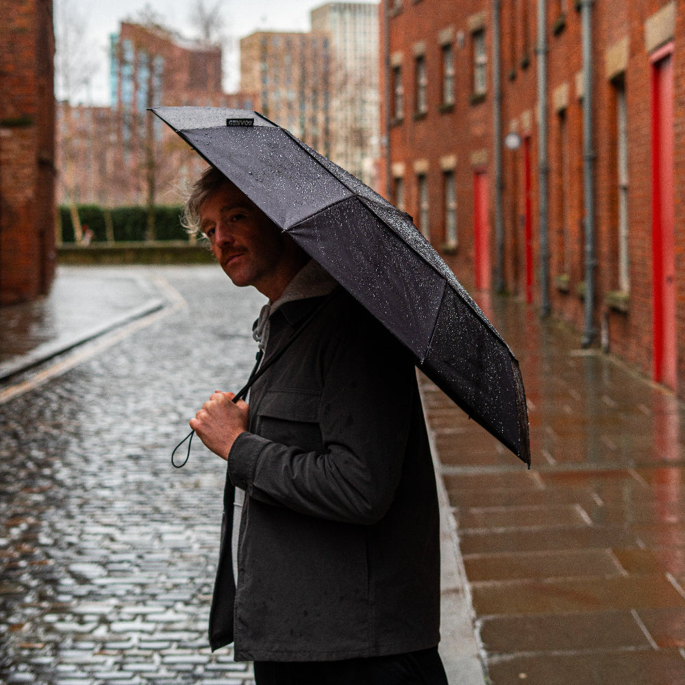 Man holding a black umbrella on a rainy street with brick buildings.