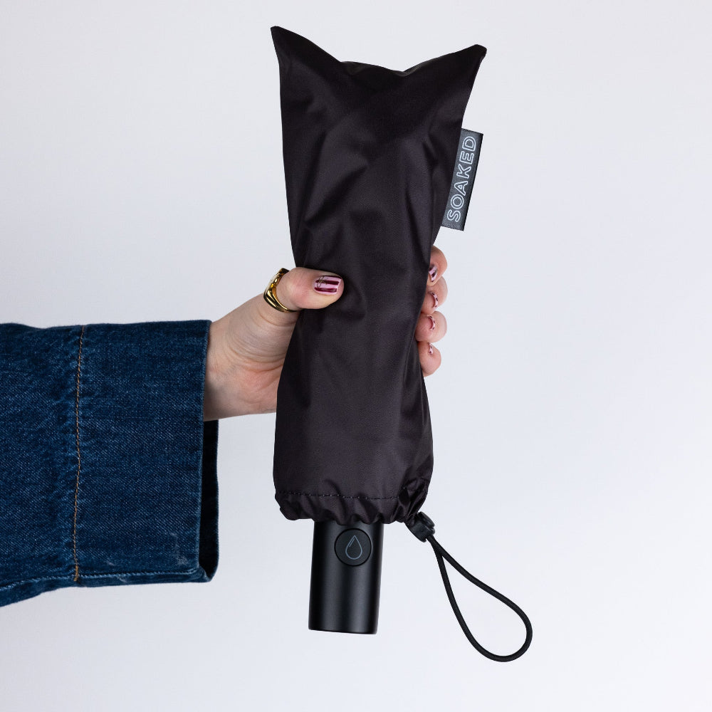 Black folded umbrella held by a hand with a white background