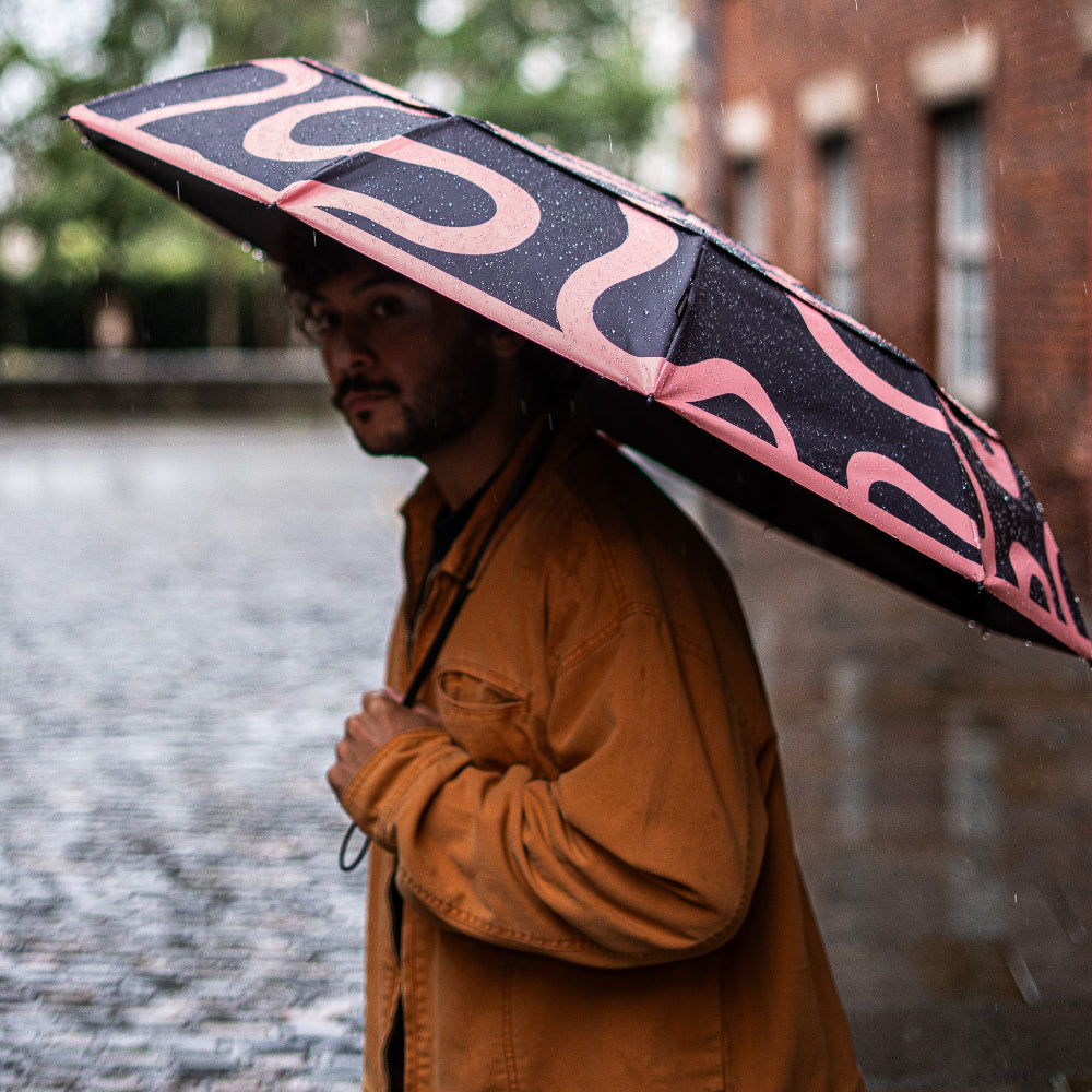 Person holding a black and pink umbrella in the rain with a blurred background