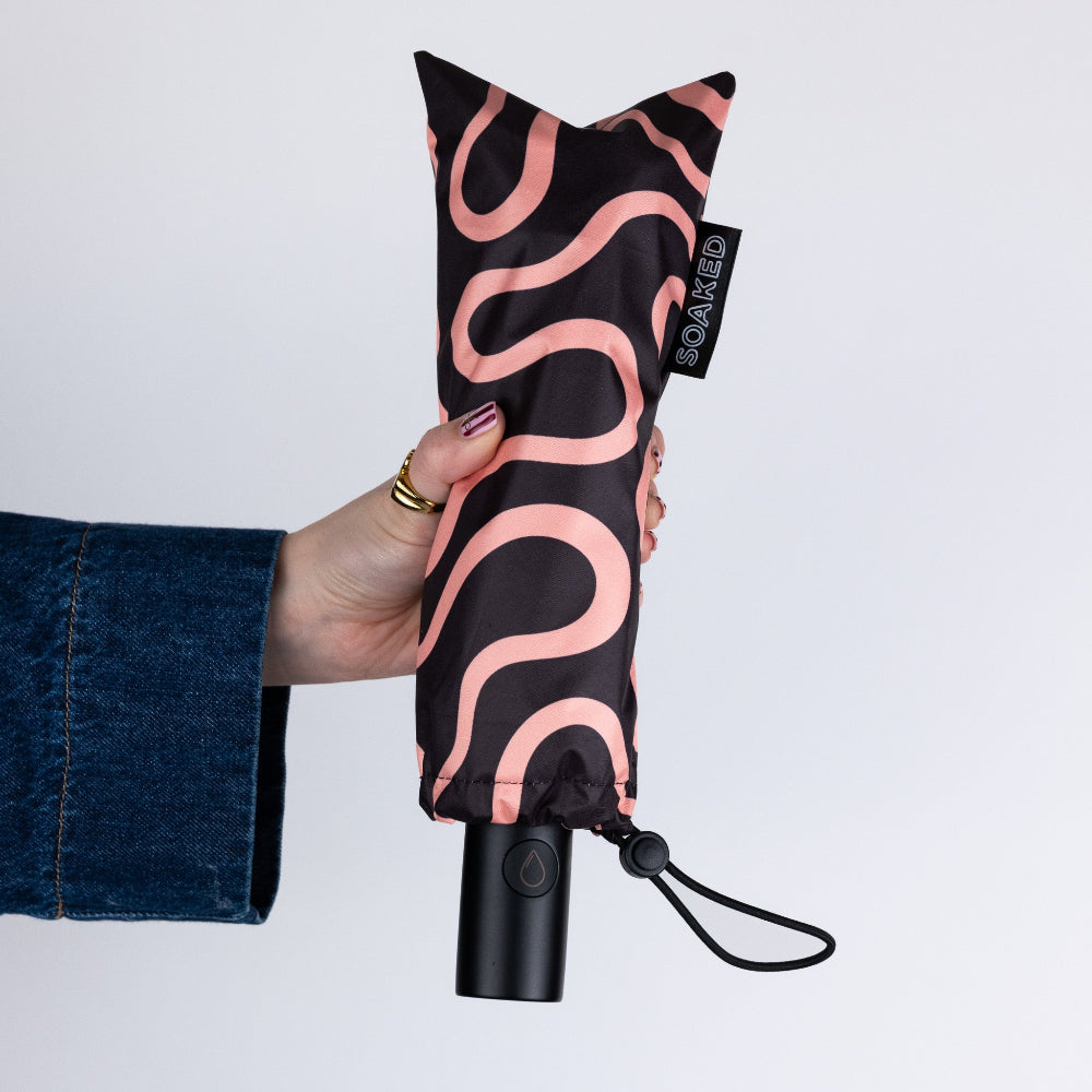 Compact umbrella with pink wave pattern held by a hand on a light gray background