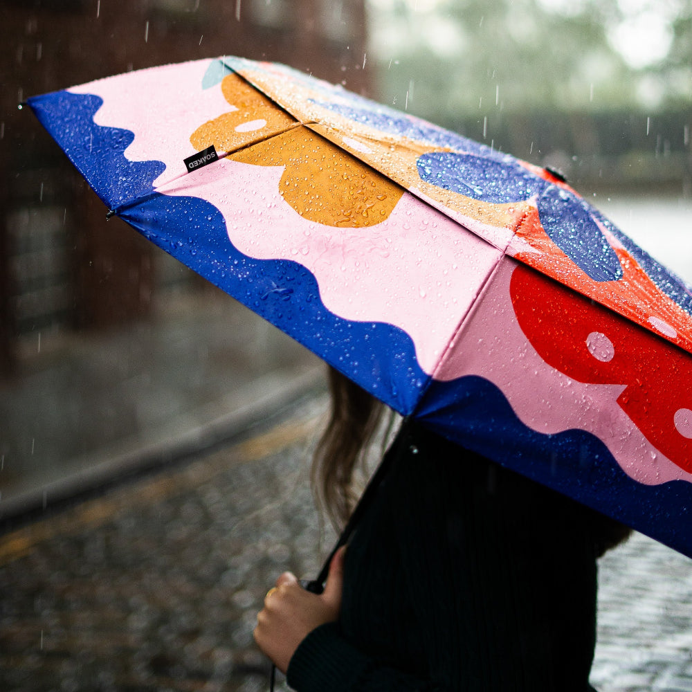 Person holding a colourful umbrella in the rain