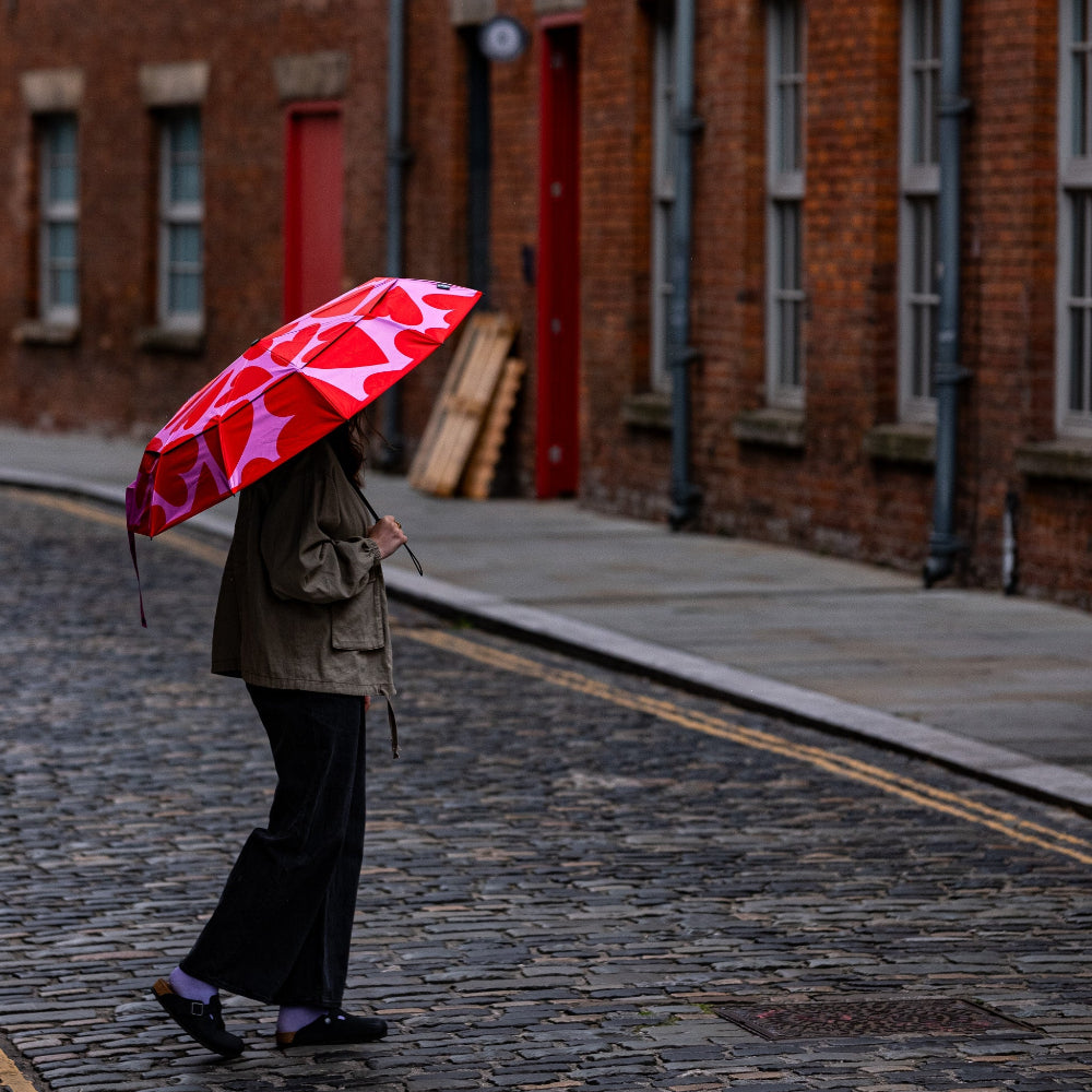 Person walking down a cobblestone street with a red and white umbrella