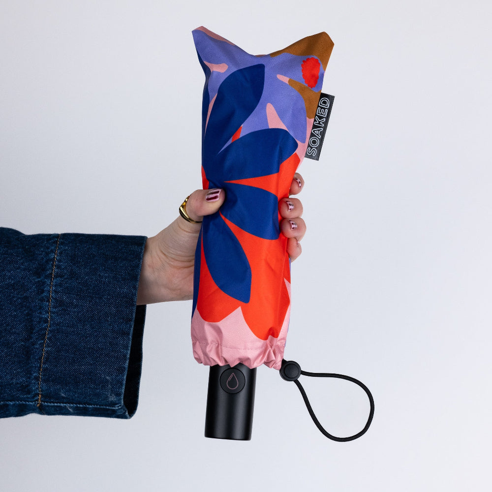 Colourful folded umbrella held by a person against a white background