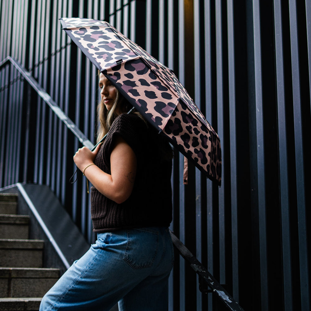Person holding a leopard print umbrella against a dark background