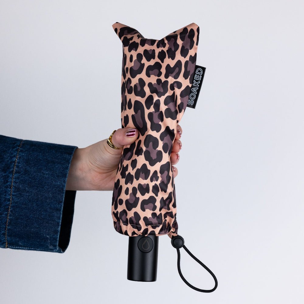 Leopard print umbrella held by a person against a white background