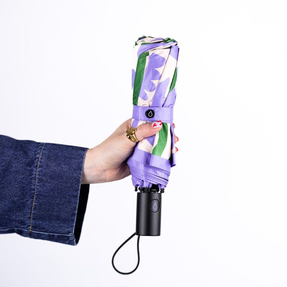 Hand holding a compact umbrella with a floral pattern on a white background