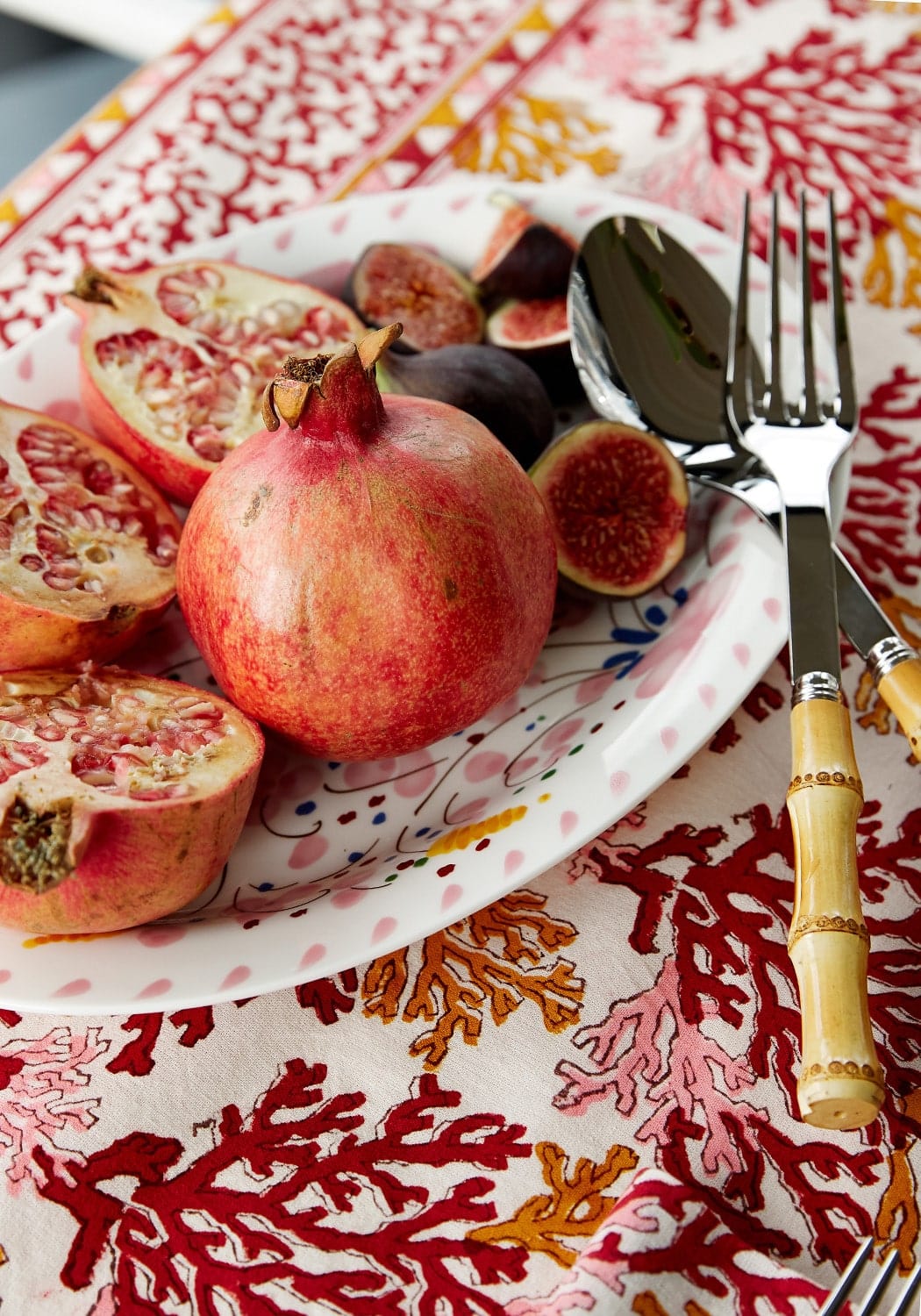 Pomegranates and figs on a plate with cutlery on a red and white patterned tablecloth.