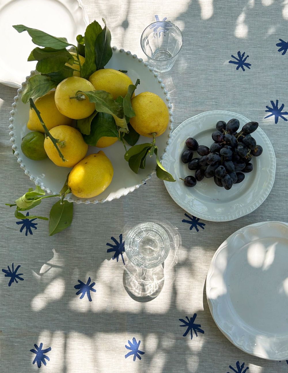 Table setting with lemons, grapes, and glasses on a tablecloth with blue star patterns.