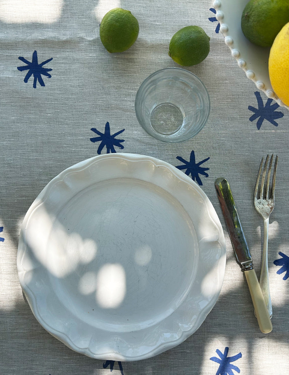 White plate on a tablecloth with blue star patterns, accompanied by a glass, knife, and fork.