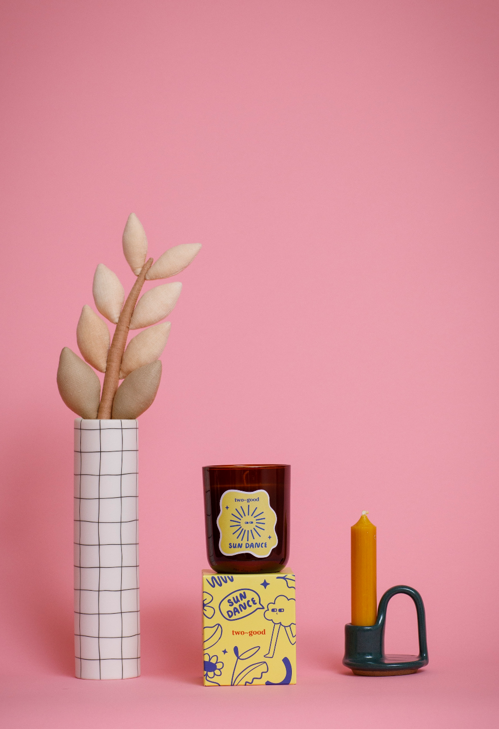Decorative items including a vase with leaves, a candle, and a small box on a pink background