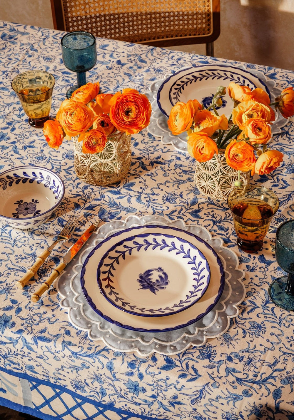 Decorative table setting with floral arrangements, plates, and glasses on a blue and white patterned tablecloth.