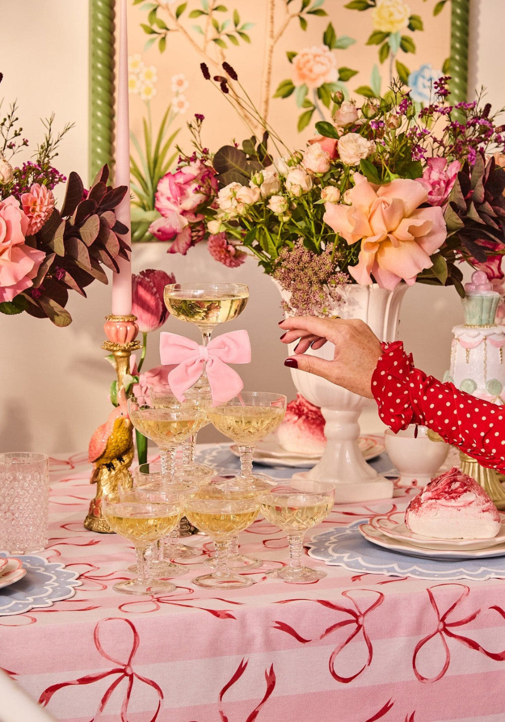 Decorative table setting with floral arrangements, glasses of champagne, and a person's hand holding a glass.