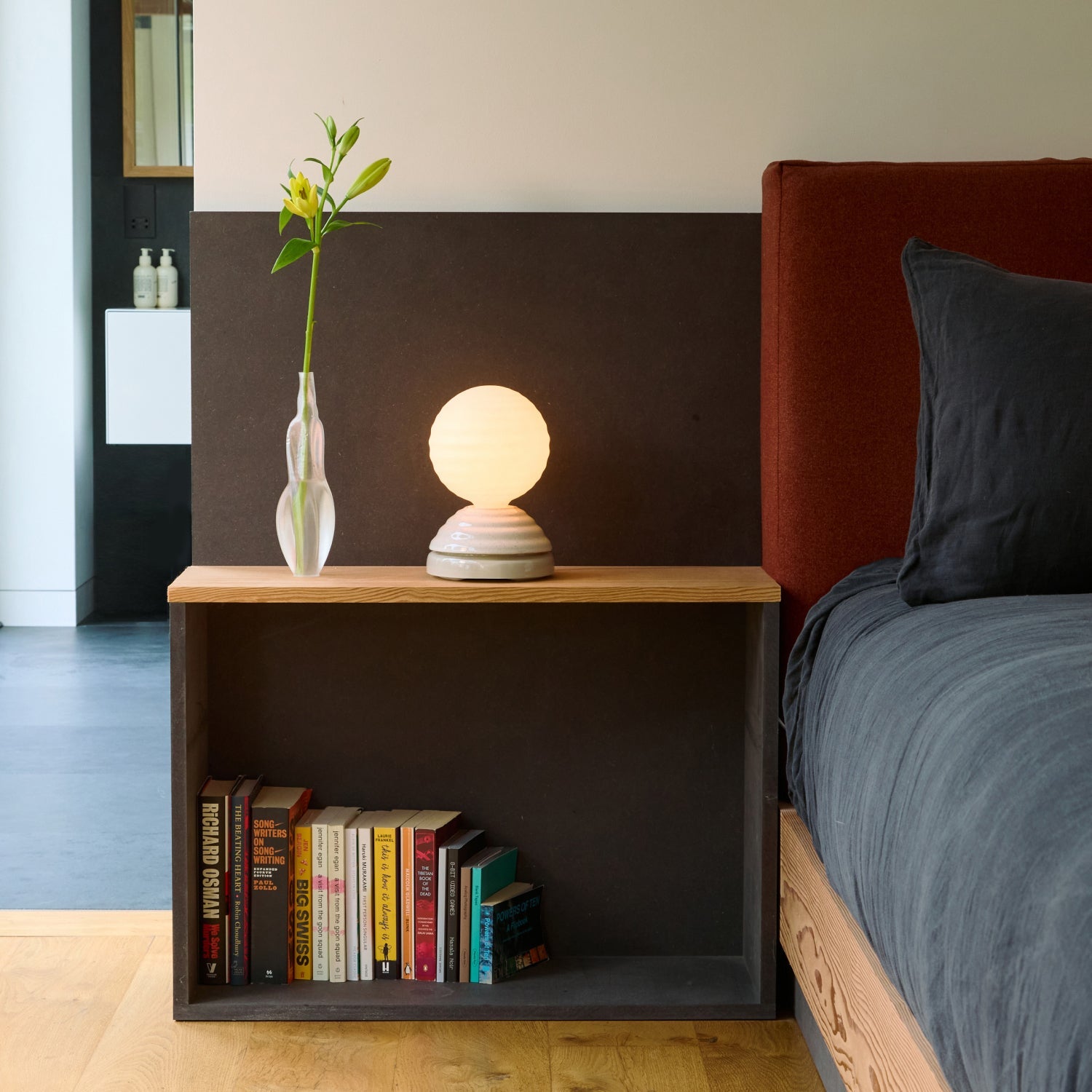 Modern bedroom with a nightstand, books, and a lamp next to a bed.