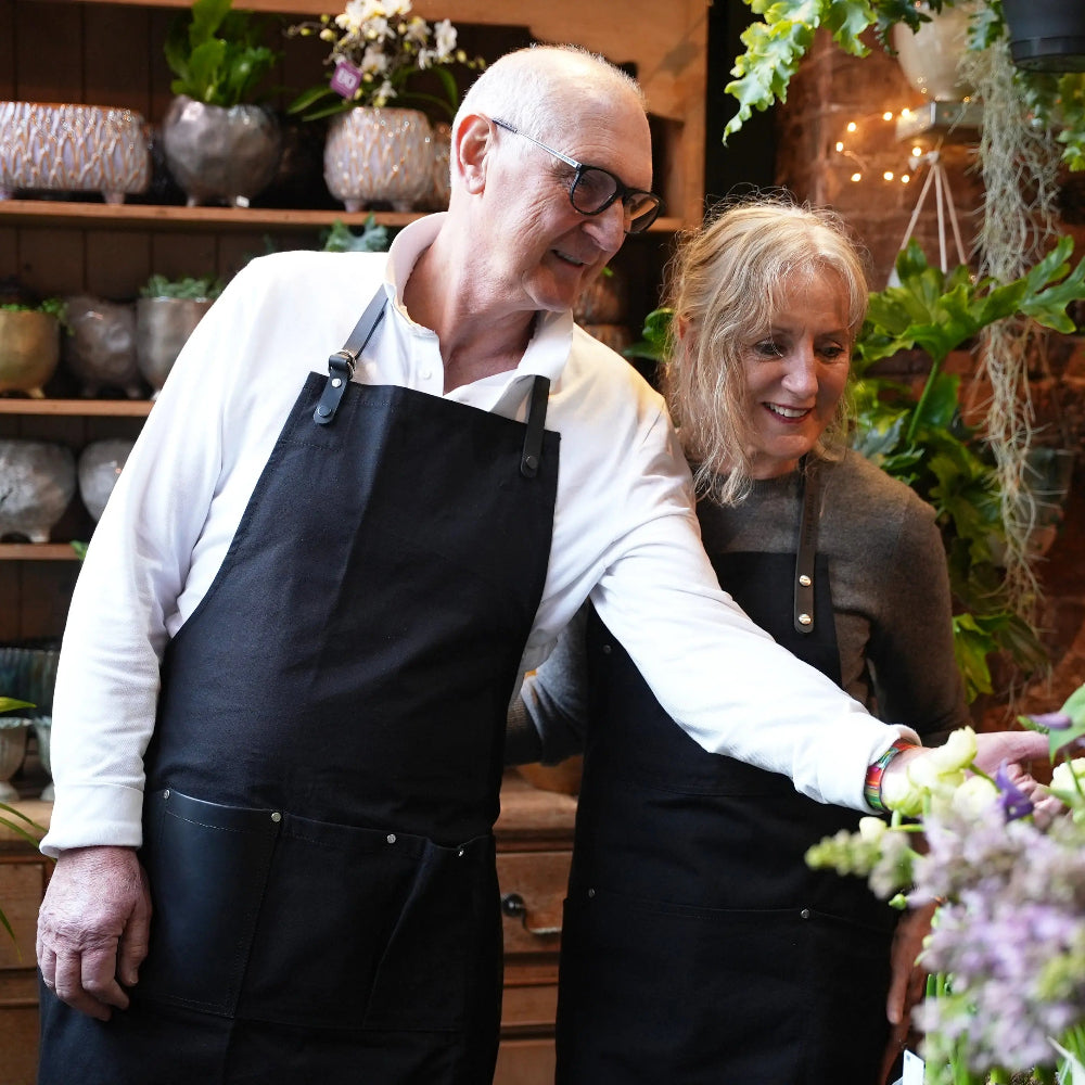 Two people wearing black aprons standing in a floral shop.