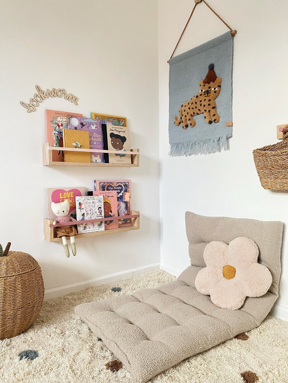 Children's room with a beige floor pillow, wall hanging, and shelves.
