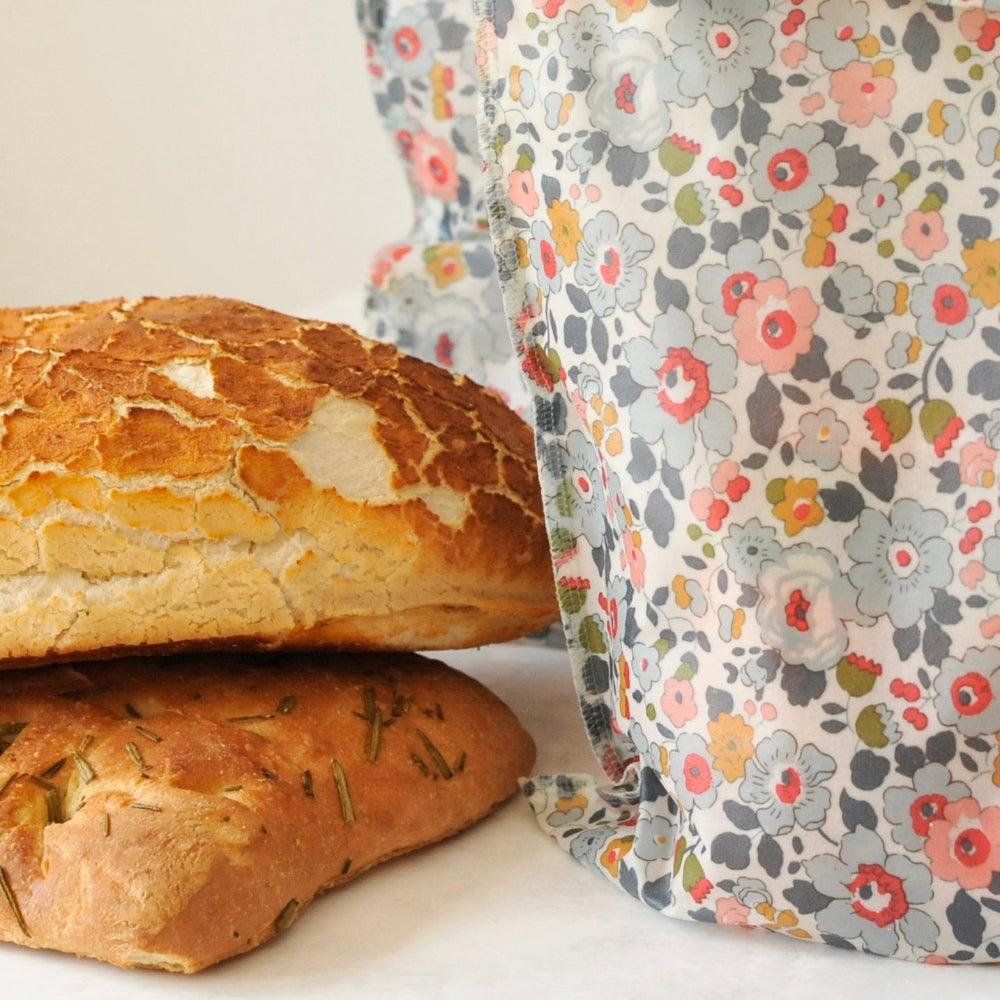 Two loaves of bread with a floral-patterned reusable bag on a light background